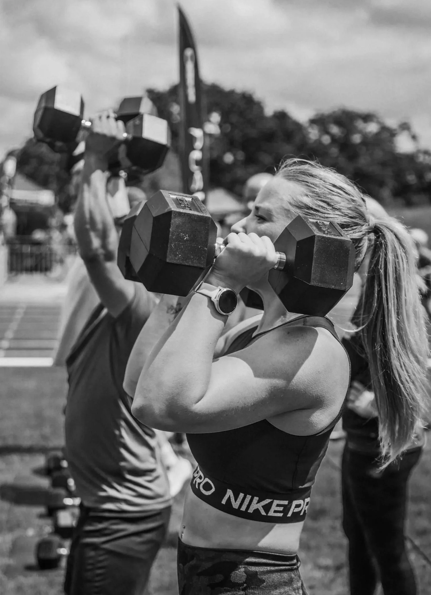 Atlet menekan dua dumbbell di atas kepala dalam Push Press Labour